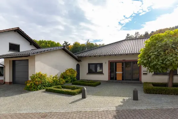 Modernes Einfamilienhaus mit gepflegtem Vorgarten, Garagenzufahrt und Baum im Vordergrund.