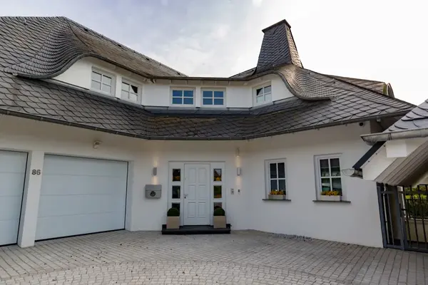 Modernes Einfamilienhaus mit auffälligem Schieferdach und gepflasterter Einfahrt.