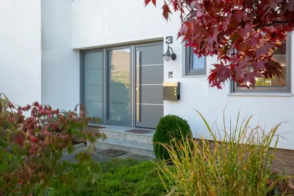 Moderne Haustür mit Glas und Edelstahlgriff, umgeben von gepflegtem Vorgarten und Herbstlaub.